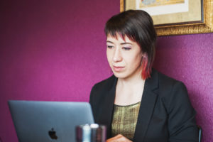 Web designer Sarah Giffrow looking at computer while sitting in front of pink wall