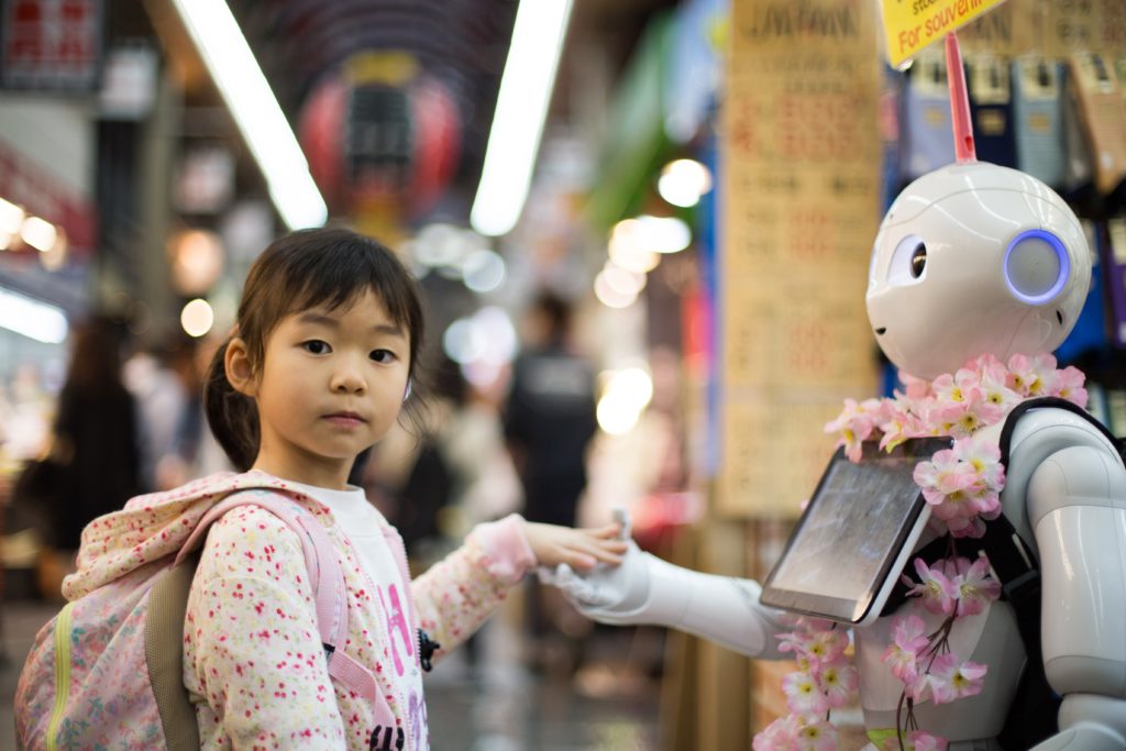 Young girl at a night market putting her hand in the hand of a robot